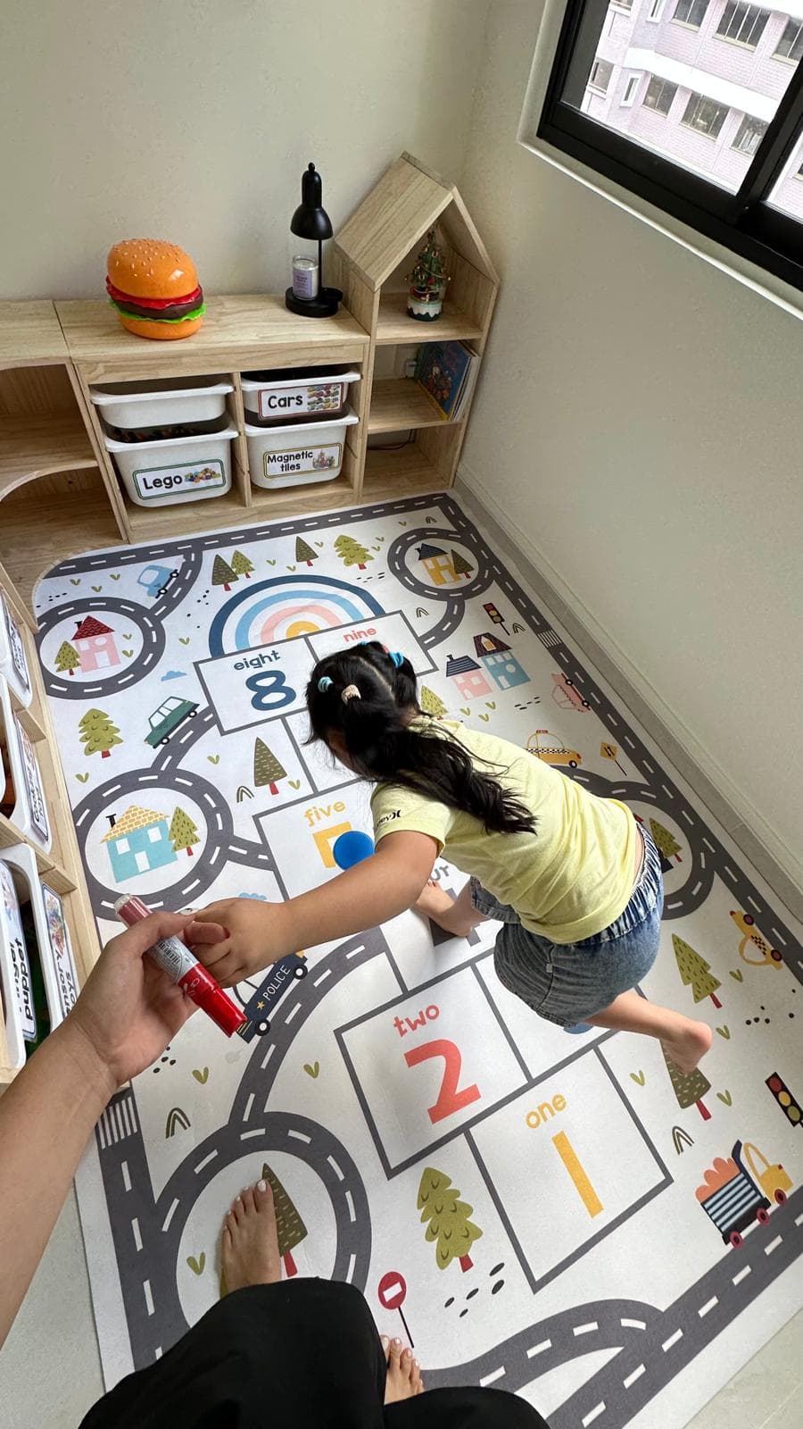 A child playing on a numbers-and-roads floor mat in the warm, home-based Inclusive Kids Club learning room